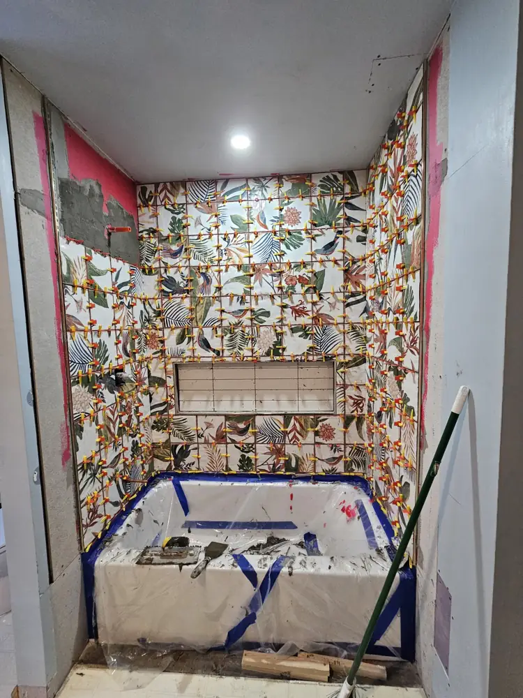 Patterned tile going up around a new tub with leveling clips in place