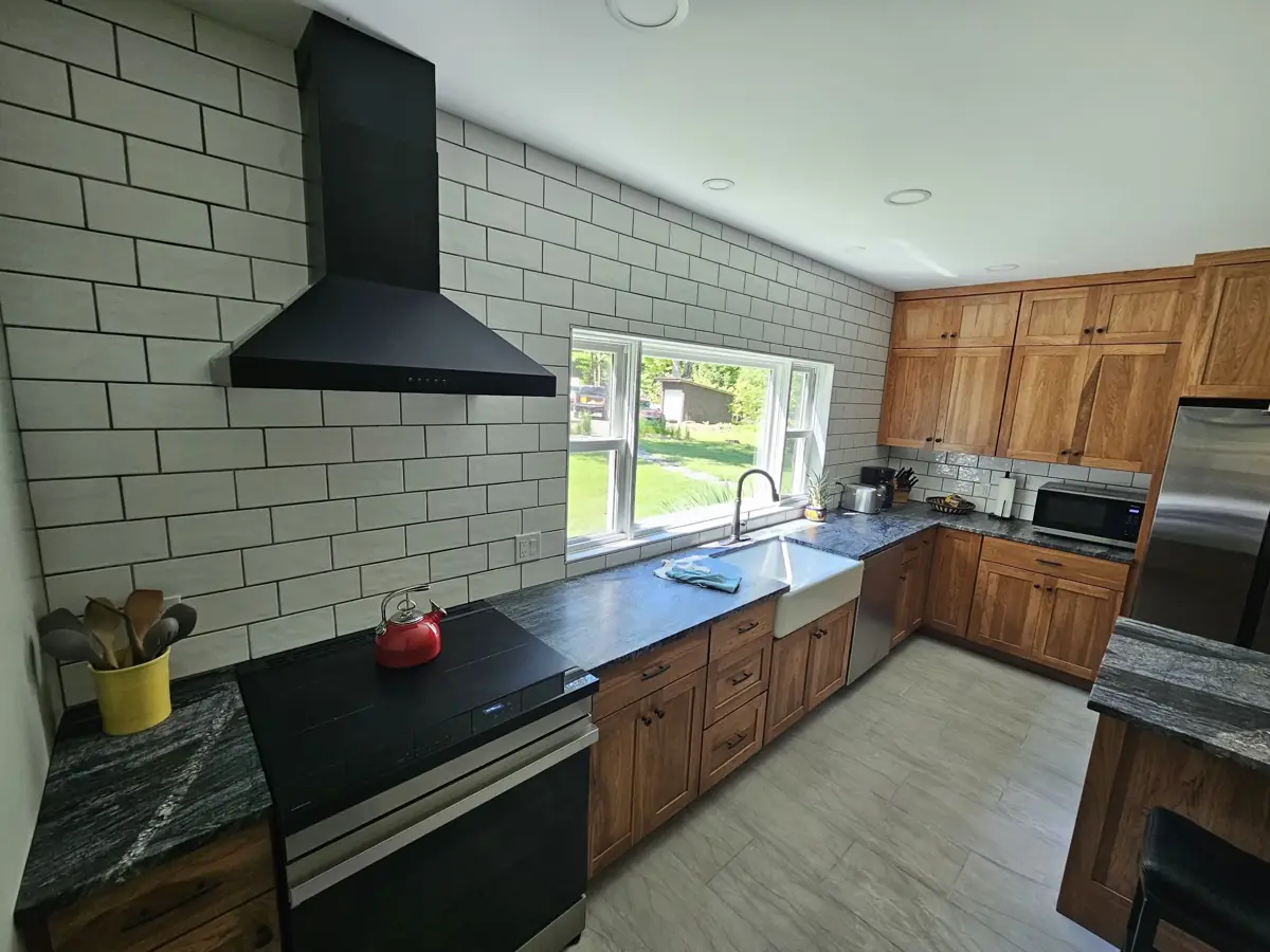 Finished kitchen with subway tile wall, black range hood and wood cabinets