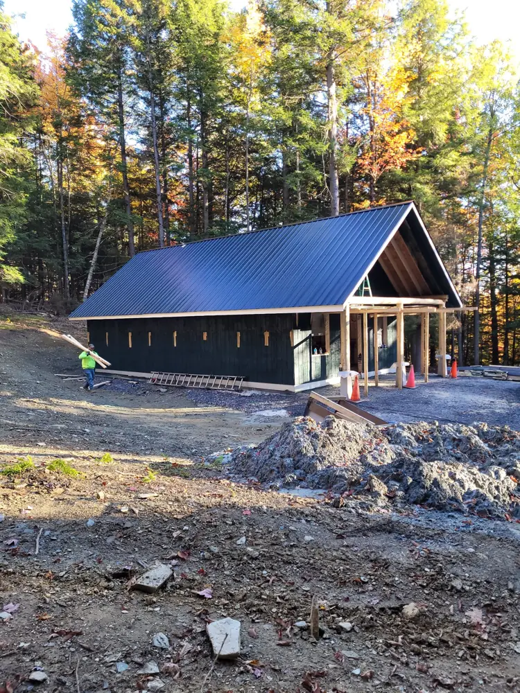 Finished building with dark green siding and log porch among fall foliage