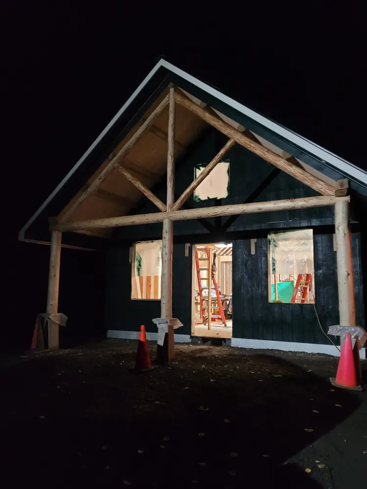 Log porch truss lit up at night against a dark green gable