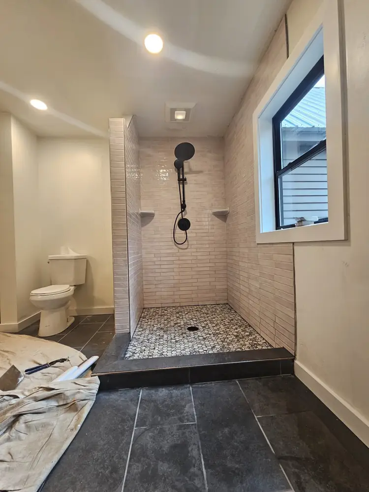 Walk-in shower with glossy long tile, marble hex floor and black rain head